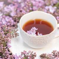 ライラックの花に囲まれた温かい紅茶とティーカップの写真