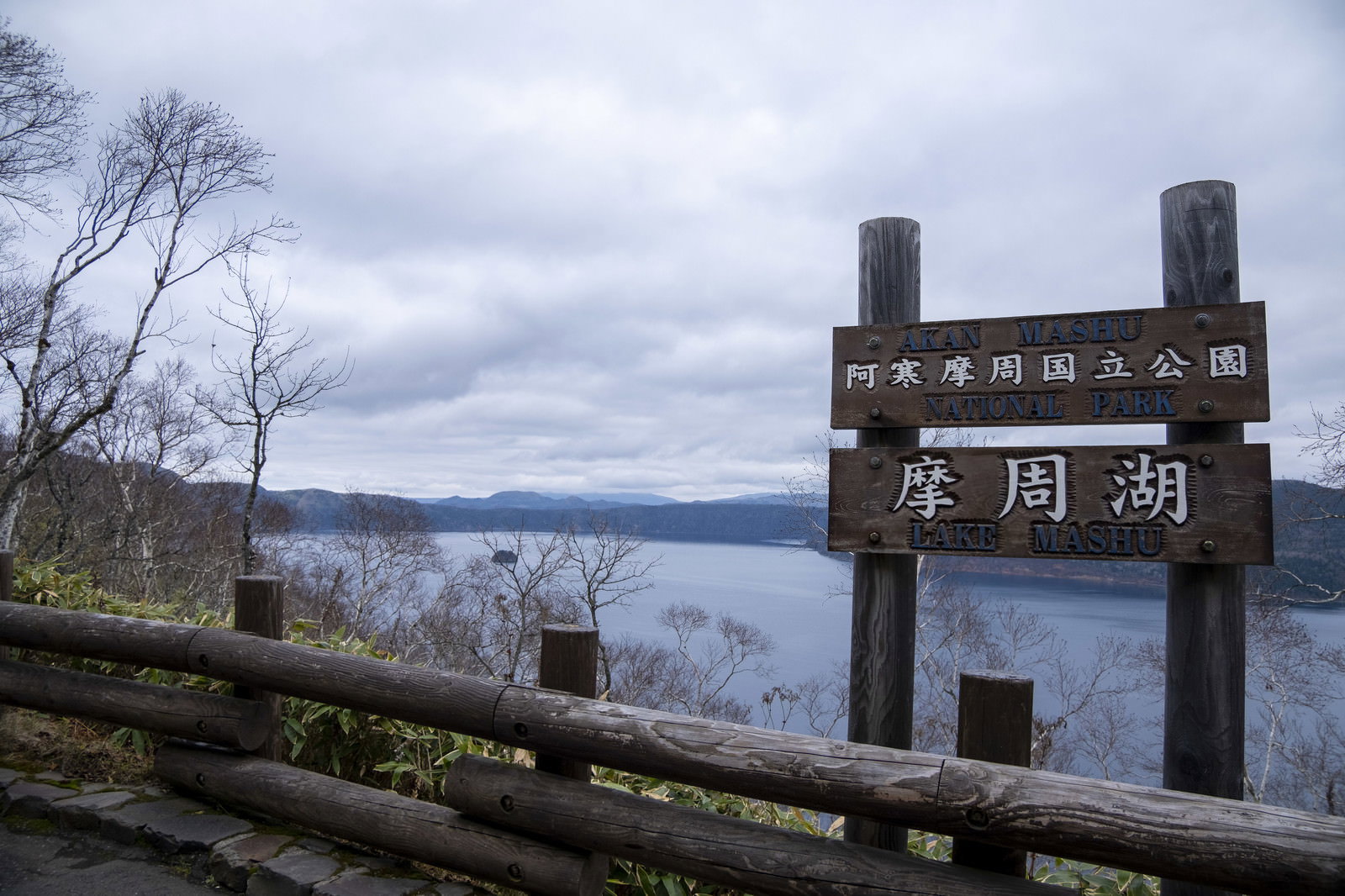 曇り空の下に立つ摩周湖展望台の木製案内看板と奥に見える湖面