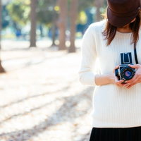クラシックカメラを手にする女子、白いニット姿で撮影の写真