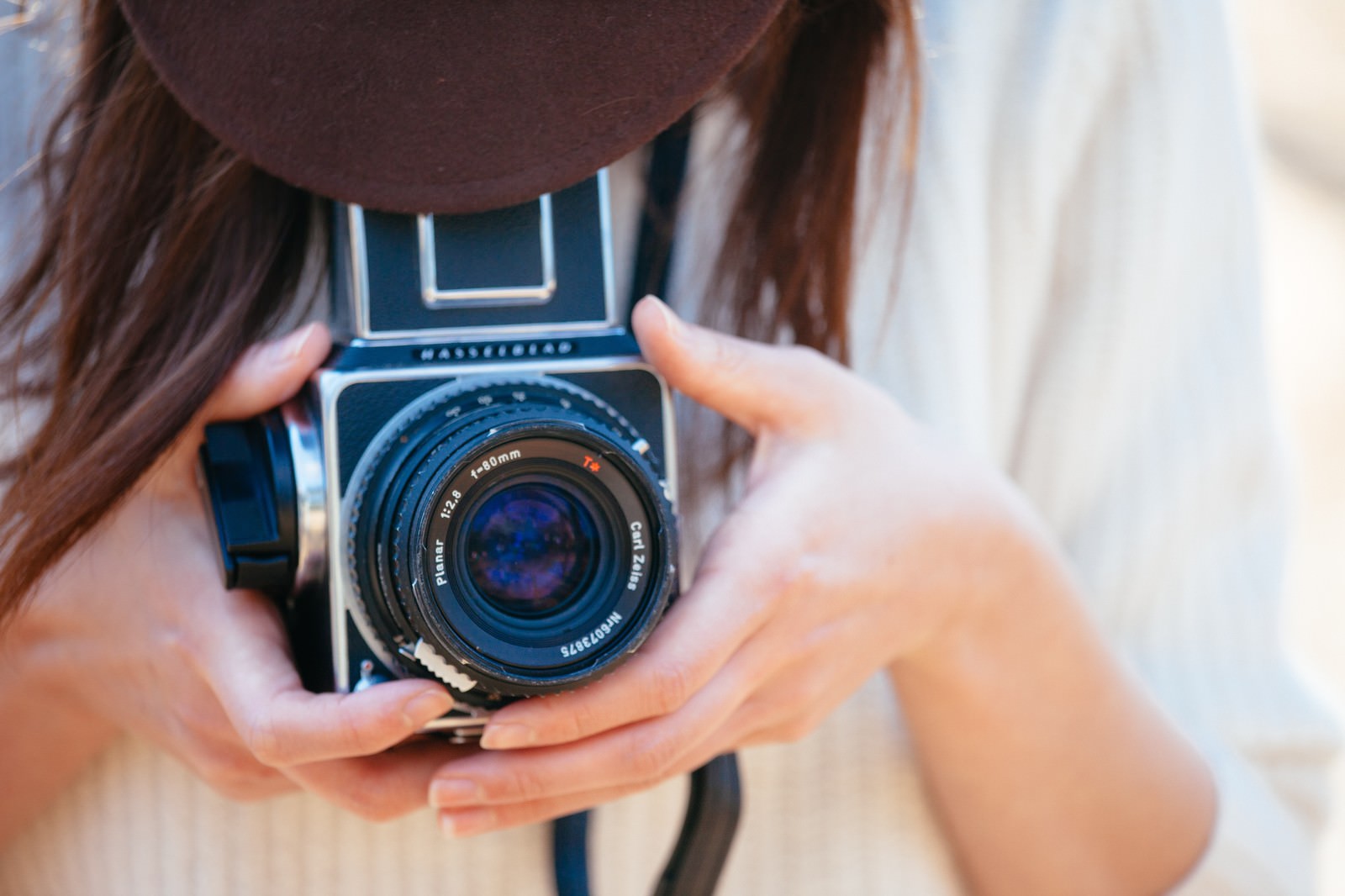 茶色い帽子をかぶり、フィルムカメラで撮影する女性