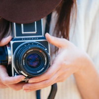 フィルムカメラで撮影する茶色い帽子の女性の写真