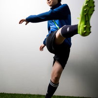 青いユニフォームの女性サッカー選手がフリーキックを決める瞬間の写真