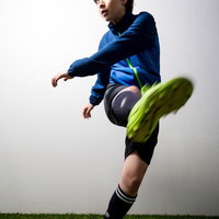 青いユニフォームの女子サッカー選手がシュートを放つ瞬間の写真