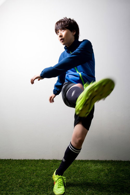 青いユニフォームの女子サッカー選手がシュートを放つ瞬間