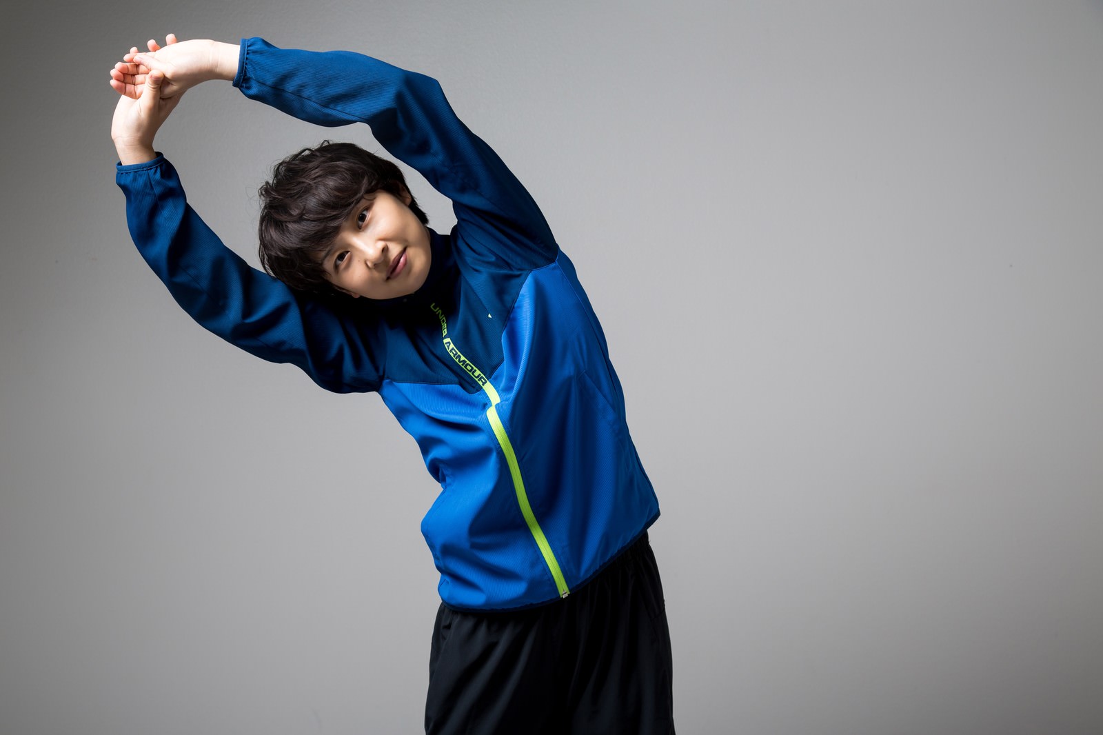 青いスポーツウェアで体を横に傾けてストレッチする子ども［モデル：八木彩香］