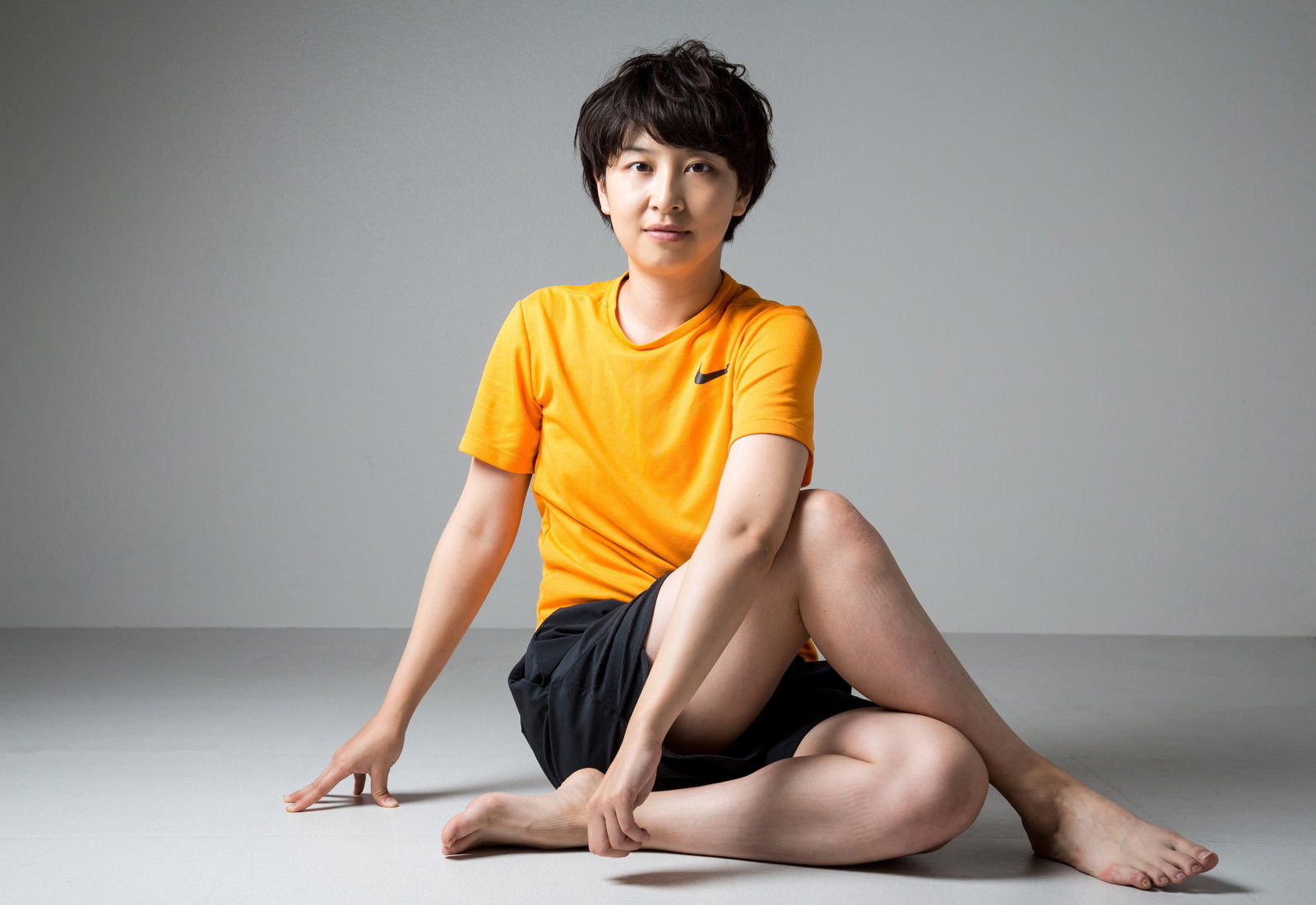 黄色いスポーツウェアで床に座りストレッチする女性［モデル：八木彩香］