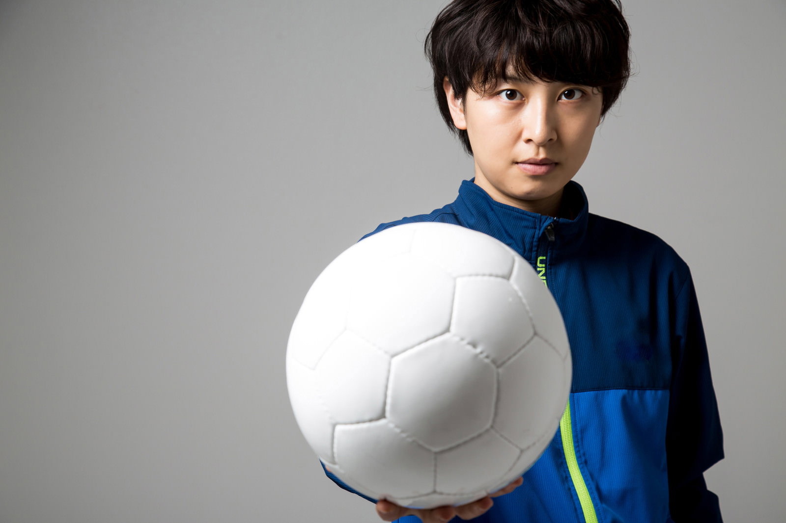 白いサッカーボールを両手で掲げる紺色ウェアの女子生徒［モデル：八木彩香］