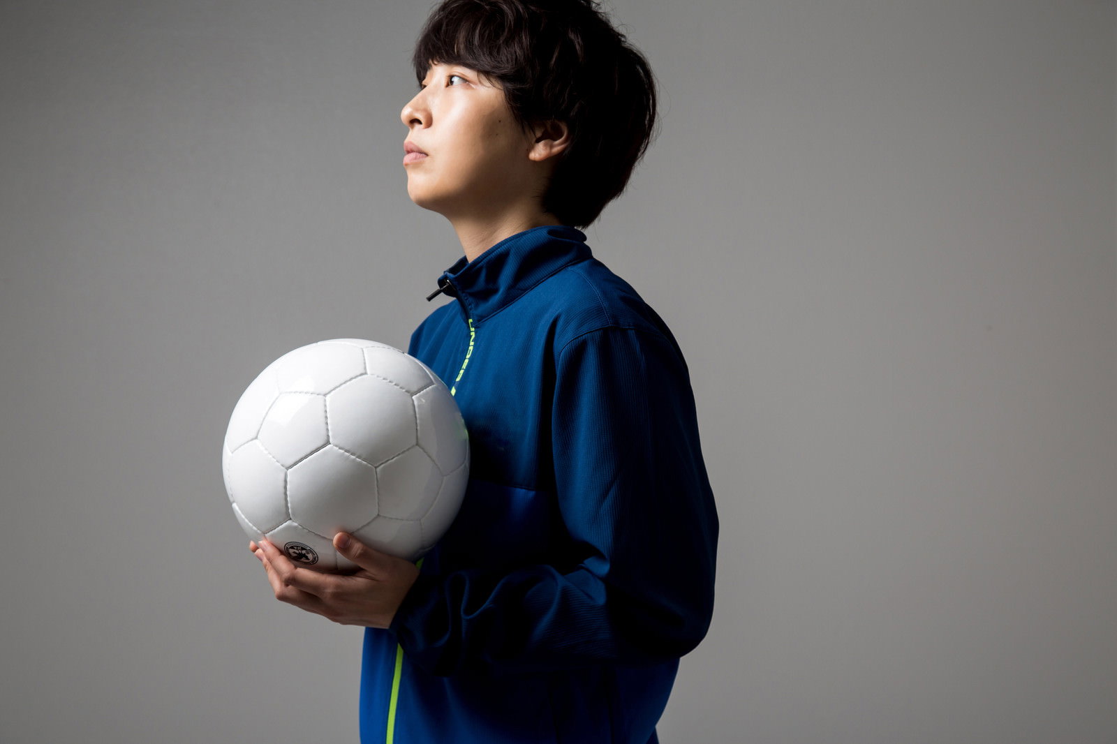 紺色のジャージを着た少年がサッカーボールを両手で抱え、視線を上方に向けている［モデル：八木彩香］
