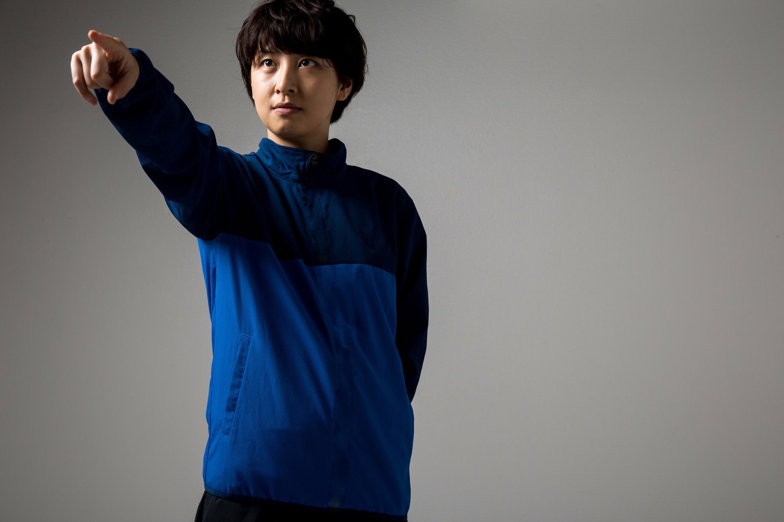 紺と青のジャージを着た女性監督が腕を伸ばして指示［モデル：八木彩香］