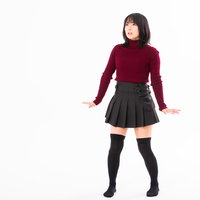 赤いニットとチェックスカート姿で後退りする女性の写真