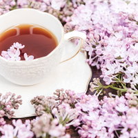 ライラックの花に囲まれた温かい紅茶とティーカップの写真