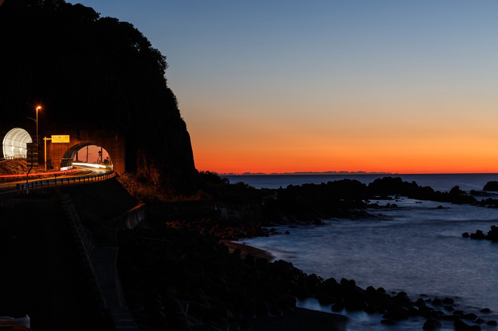 夕焼け空の下、海岸沿いの道路とトンネルのシルエット