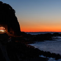 日没の日本海と沿岸の道路を走るトンネルと夕焼け風景の写真