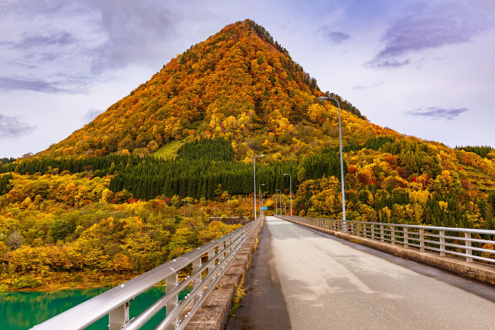秋の紅葉に彩られたとんがり山と湖にかかる橋の風景