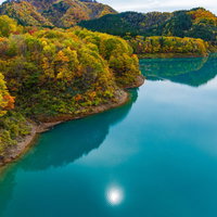 紅葉に囲まれたダム湖に反射する太陽と秋の風景の写真