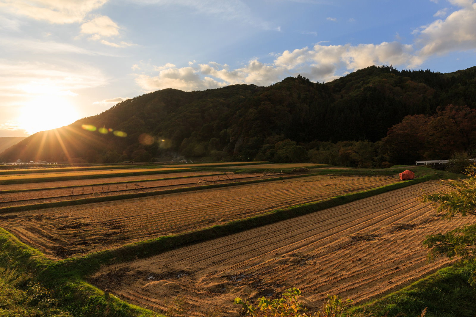 夕日が山の向こうに沈む稲刈り後の田んぼと雲が浮かぶ空