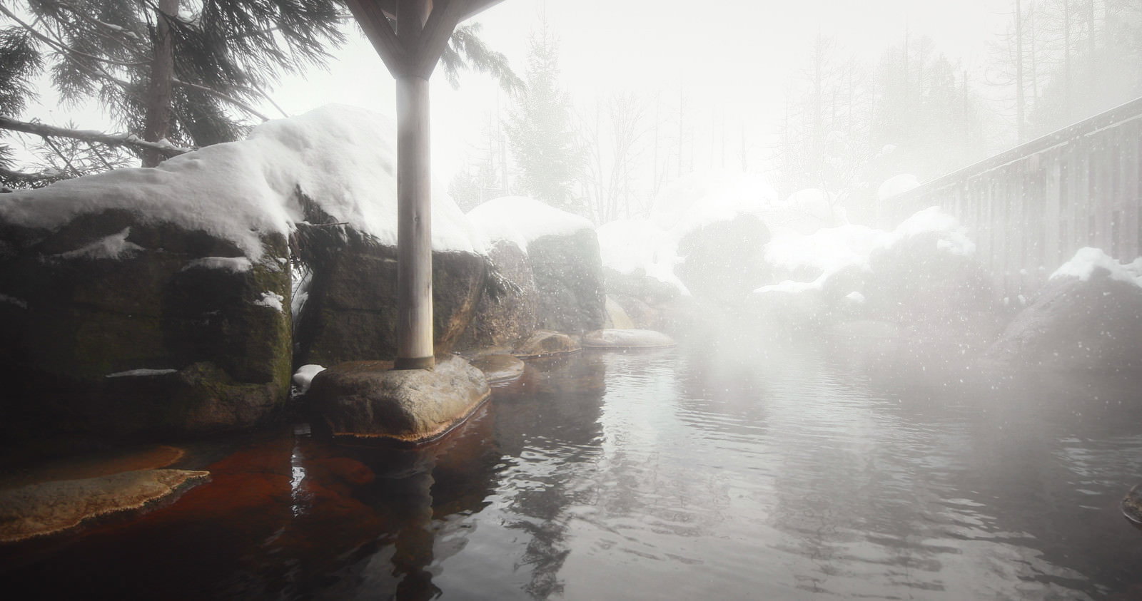 Outdoor hot spring bath with steam rising and a snowy landscape