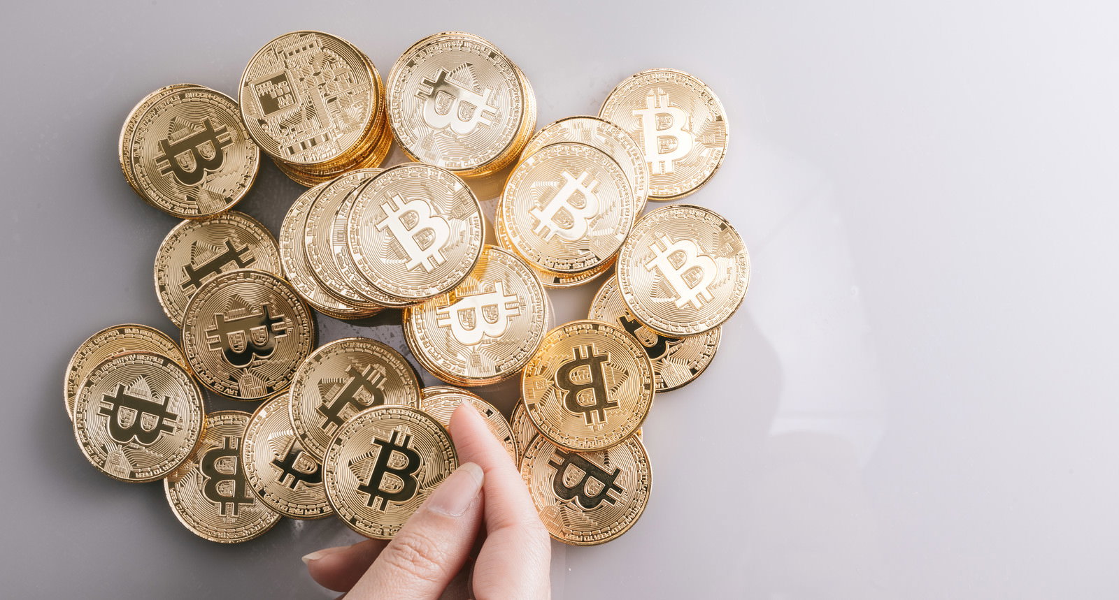 白い背景に散らばるビットコインの金貨を手で指し示している様子