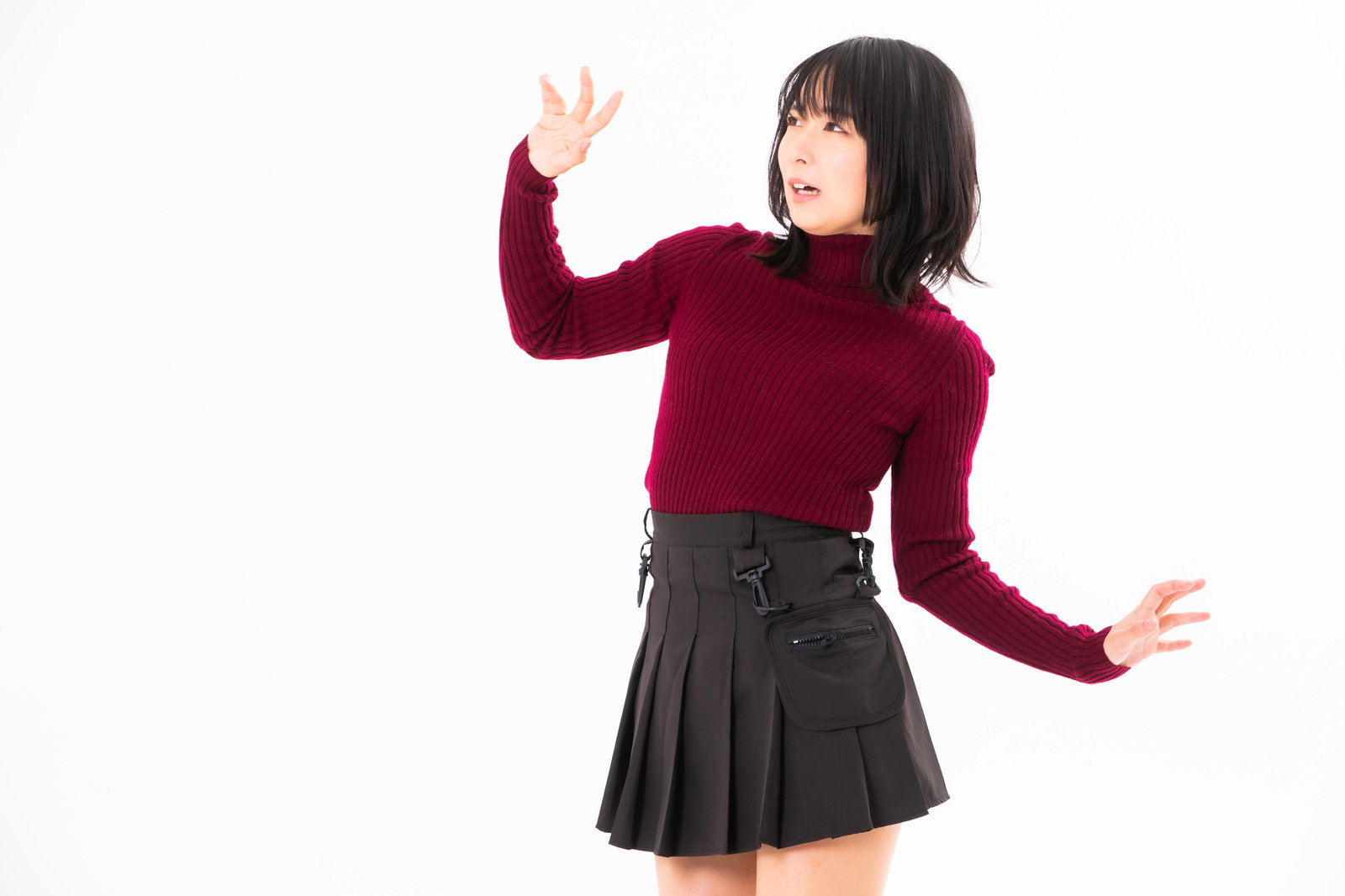 赤いセーターと黒いスカートを着た女性が両手を上げて後ずさりしている［モデル：にゃるる］