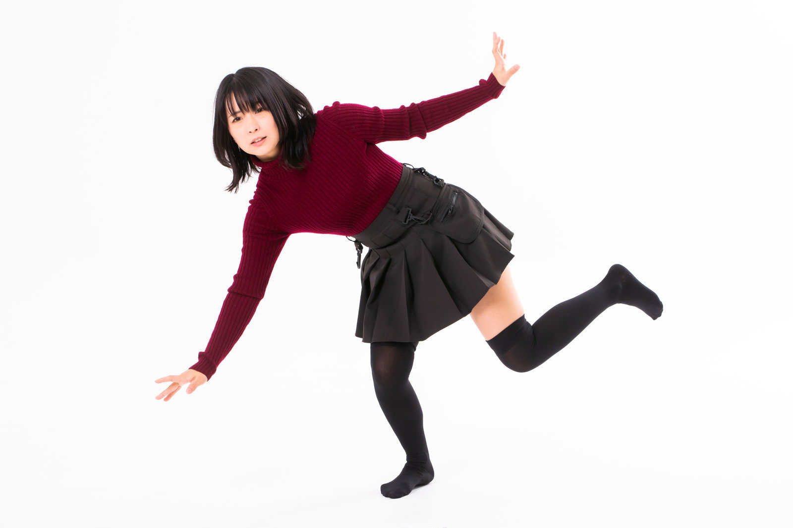 エンジ色のセーターと黒いスカートを着た女性が躓いてバランスを崩している様子［モデル：にゃるる］