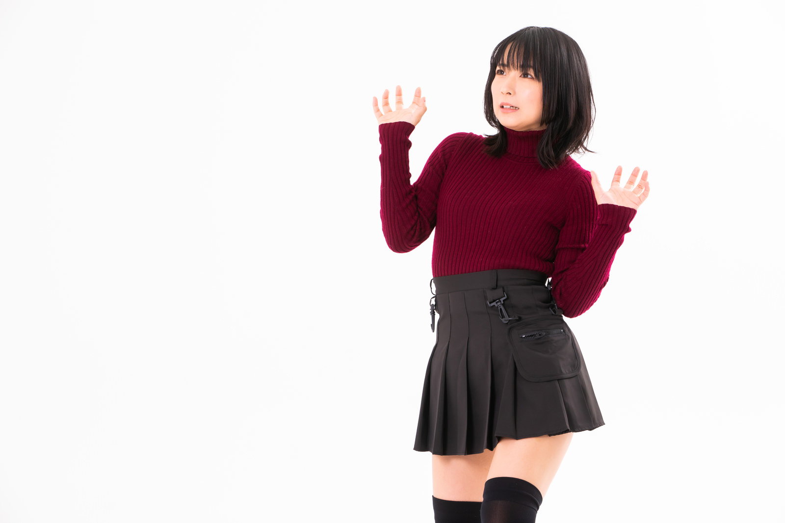 赤いセーターと黒いスカートを着た女性が両手を上げて萎縮するポーズ［モデル：にゃるる］