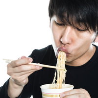 箸でカップラーメンをすする男性の食事風景の写真