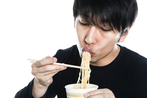 箸でカップラーメンをすする男性の食事風景