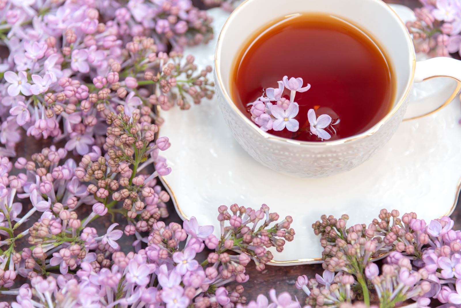淡い紫色のライラックの花弁が浮かぶ紅茶入りのティーカップ