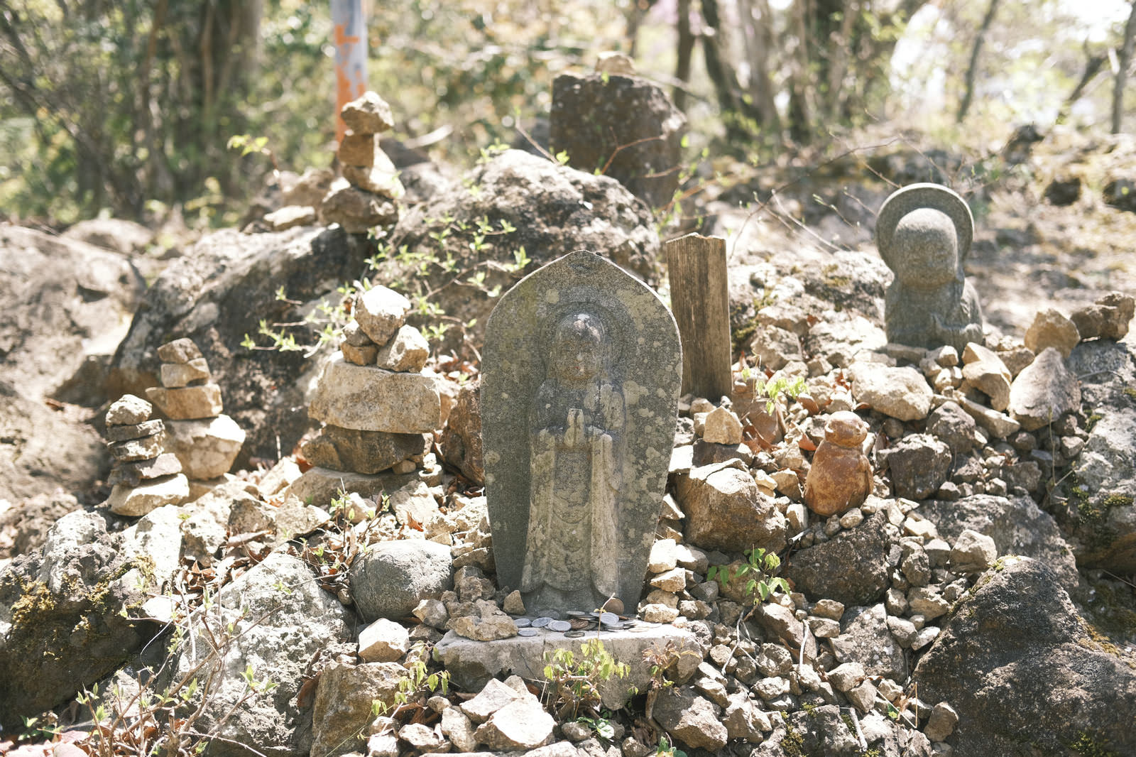 山の岩場に立つ地蔵菩薩と積み石