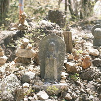 山中の岩場に立つお地蔵さんと積み石の写真