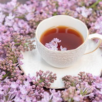 ライラックの蕾に囲まれるハーブティーのティーカップの写真