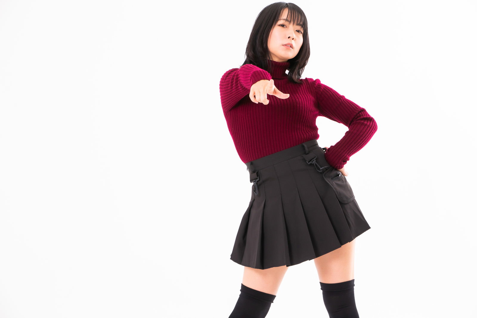 腰に手を当てて指差しポーズをとる赤いニットの女性［モデル：にゃるる］