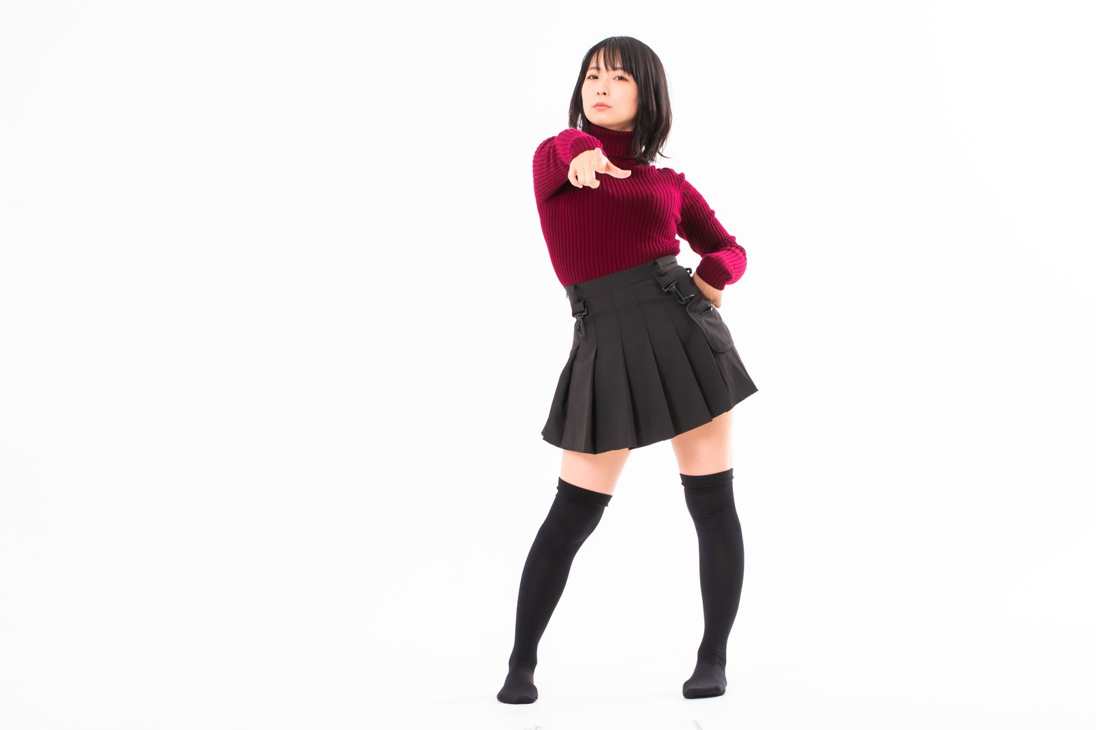 紅色のセーターと黒いプリーツスカートを着た女性が指を差して犯人を指摘するポーズ［モデル：にゃるる］