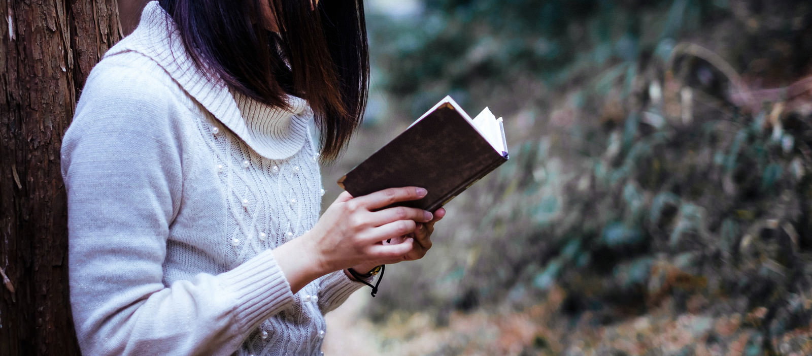 白いニットを着た女性が本を手に持って読んでいる