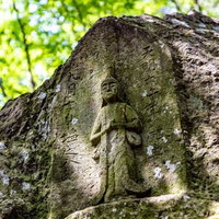武石公園の木々に包まれる苔むした石像に差し込む木漏れ日の写真