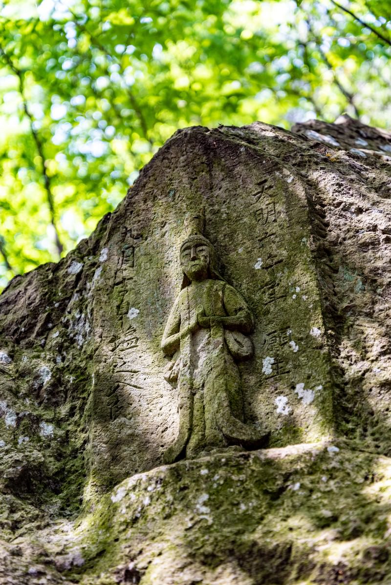緑の木々に囲まれ、木漏れ日が差し込む中に佇む苔むした石の観音像