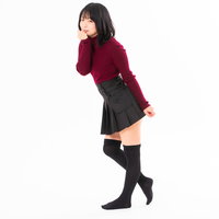 ワインレッドニットと黒プリーツスカートでうふふと微笑む女性の写真