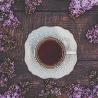 木製テーブルに俯瞰したライラックとティーカップの紅茶の写真