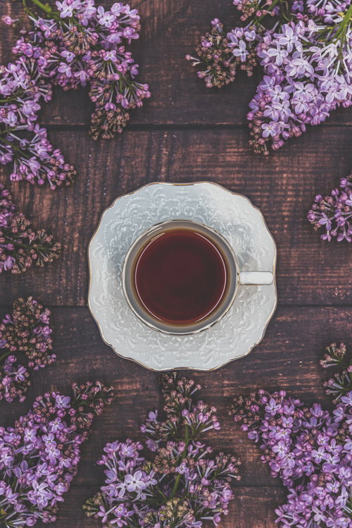 木製テーブルに俯瞰したライラックとティーカップの紅茶
