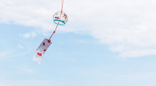 青空を背景に風で揺らぐ小さな風鈴の涼しげな風物詩