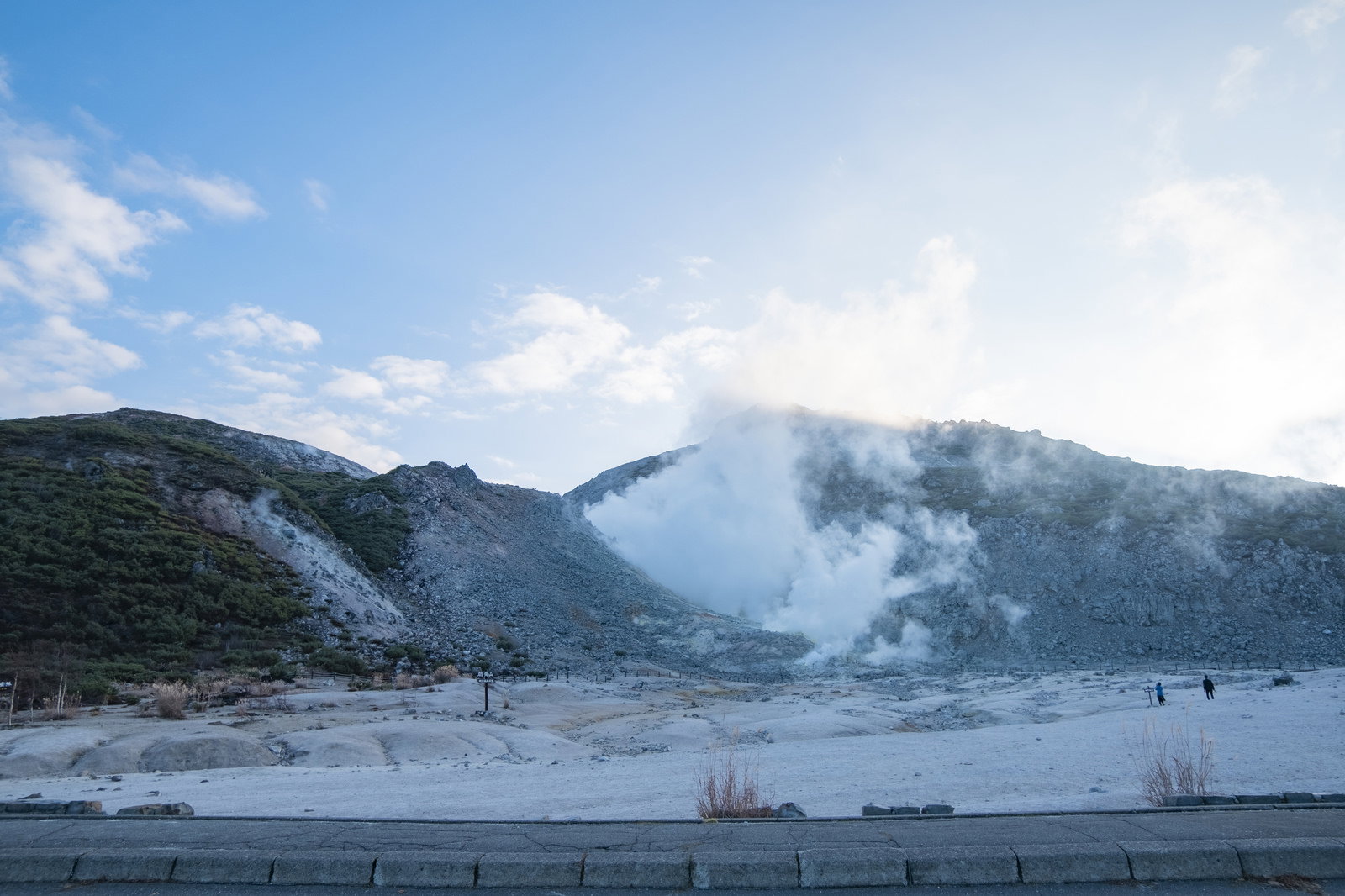 青空の下、茶褐色の山肌から白い噴煙が立ち上る北海道硫黄山の風景