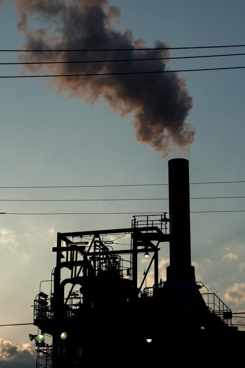 工場の煙突から立ち上る黒い排煙とシルエット