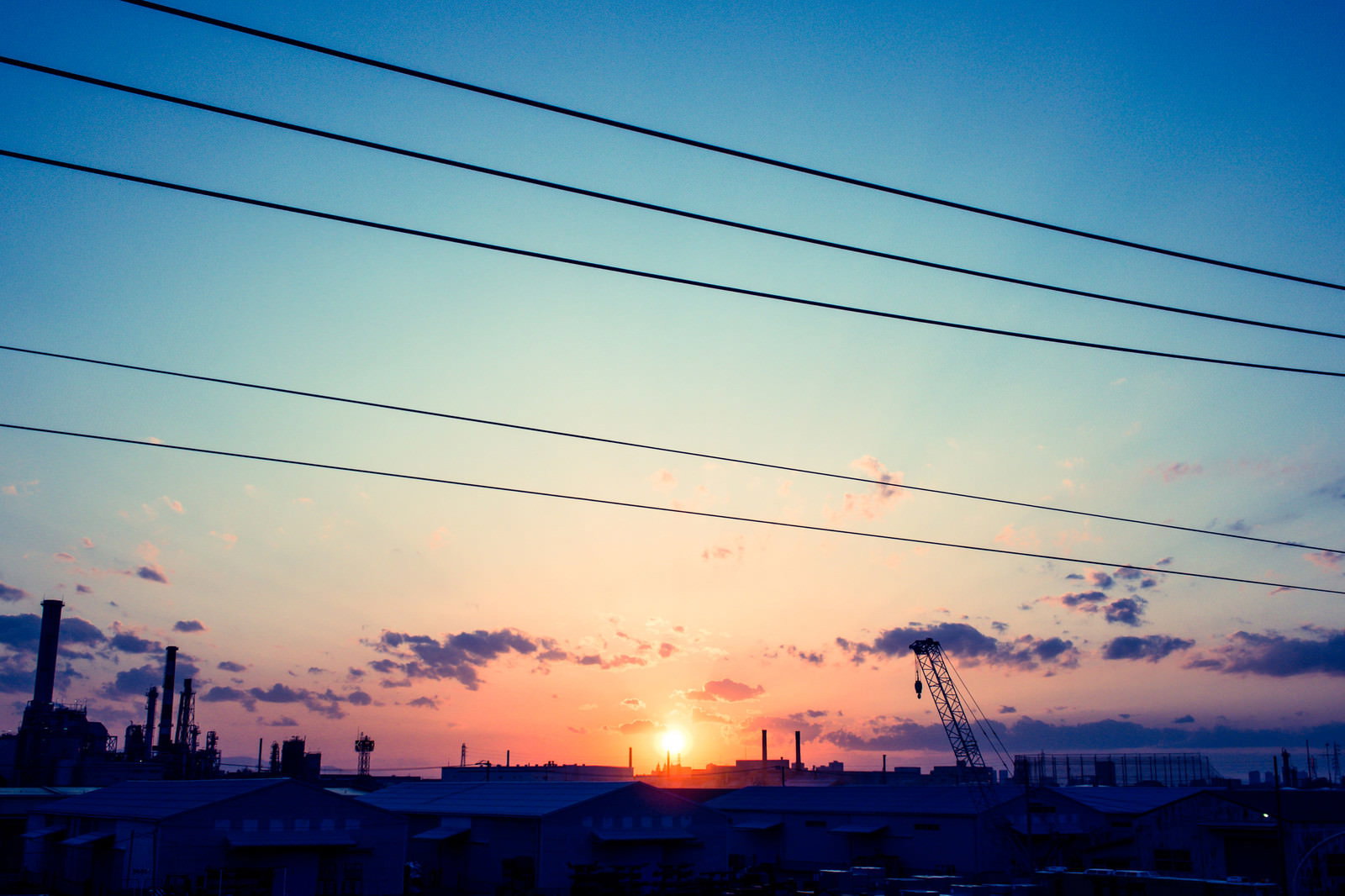 工場地帯のシルエットを背景に、電線越しに昇る日の出と太陽