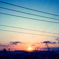 工場地帯に昇る日の出、電線と煙突のシルエット、朝焼けの太陽の写真