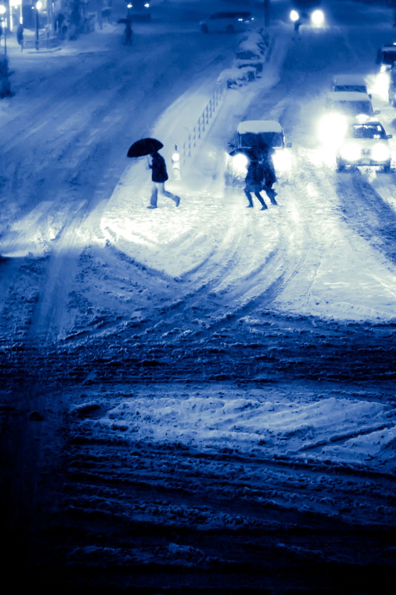 大雪の夜間都心で傘を差して歩く人と積雪した道路