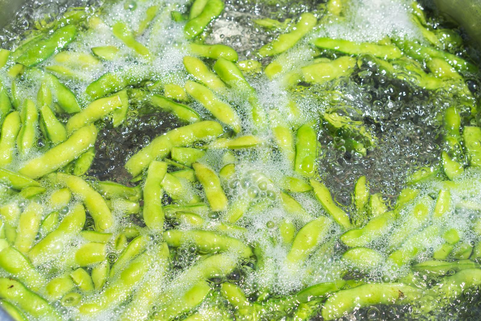 鍋の中で沸騰したお湯に入れられて茹でられている緑色の枝豆