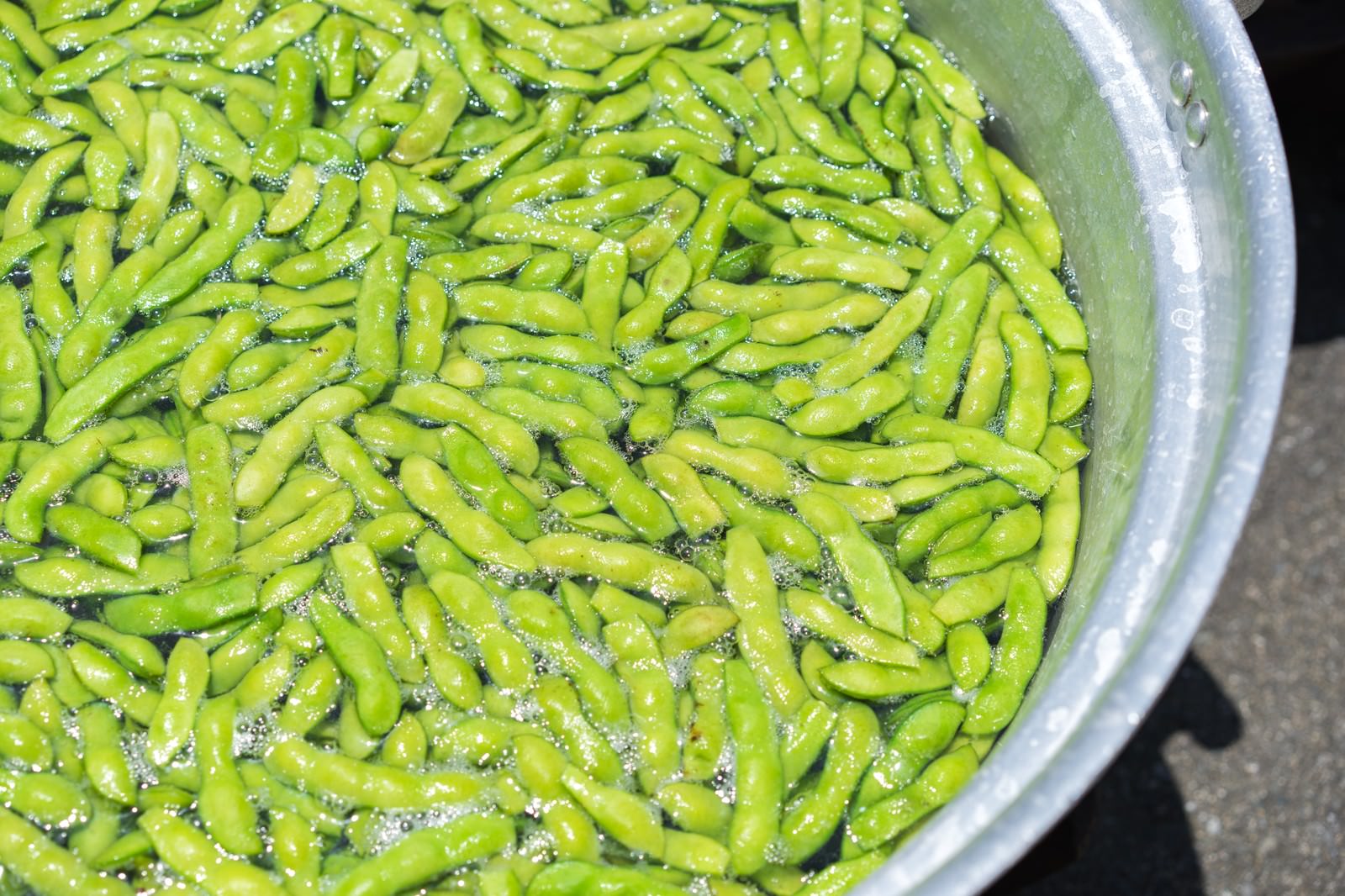 白い鍋で茹でられた緑色の枝豆がたっぷりと入っている様子