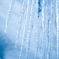 透明な氷柱に差し込む冬の日の光と青空の写真