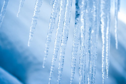 透明な氷柱に差し込む冬の日の光と青空