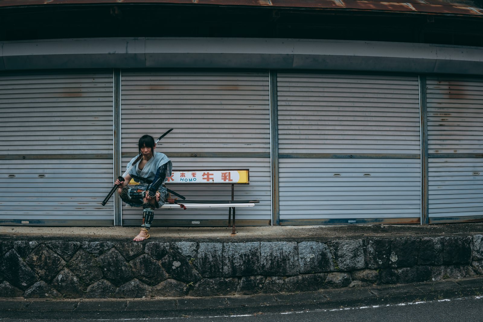 グレーのシャッター前のベンチに座って休憩する男性［モデル：まーこ］